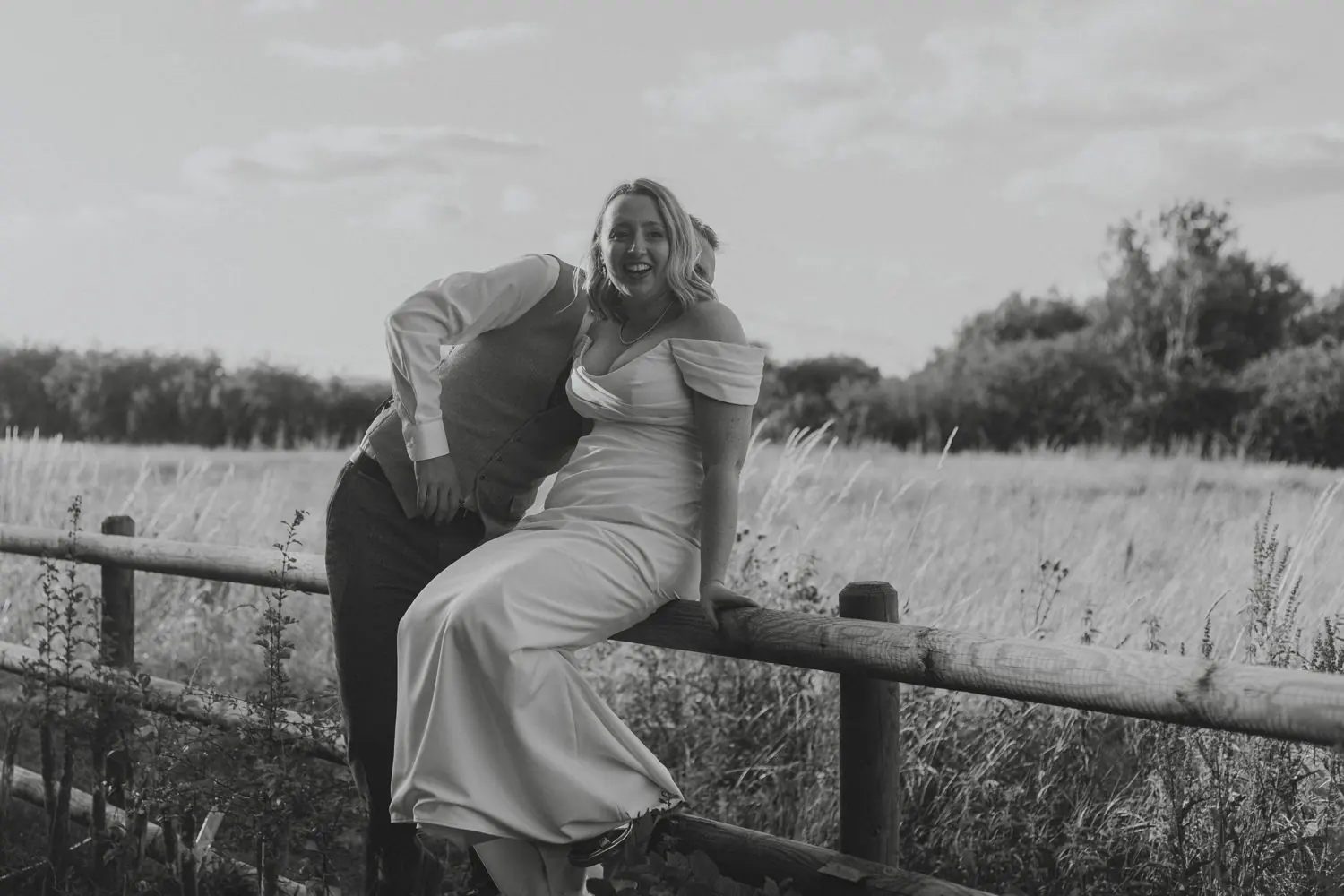 Couple laughing together on a fence in a field, in black and white
