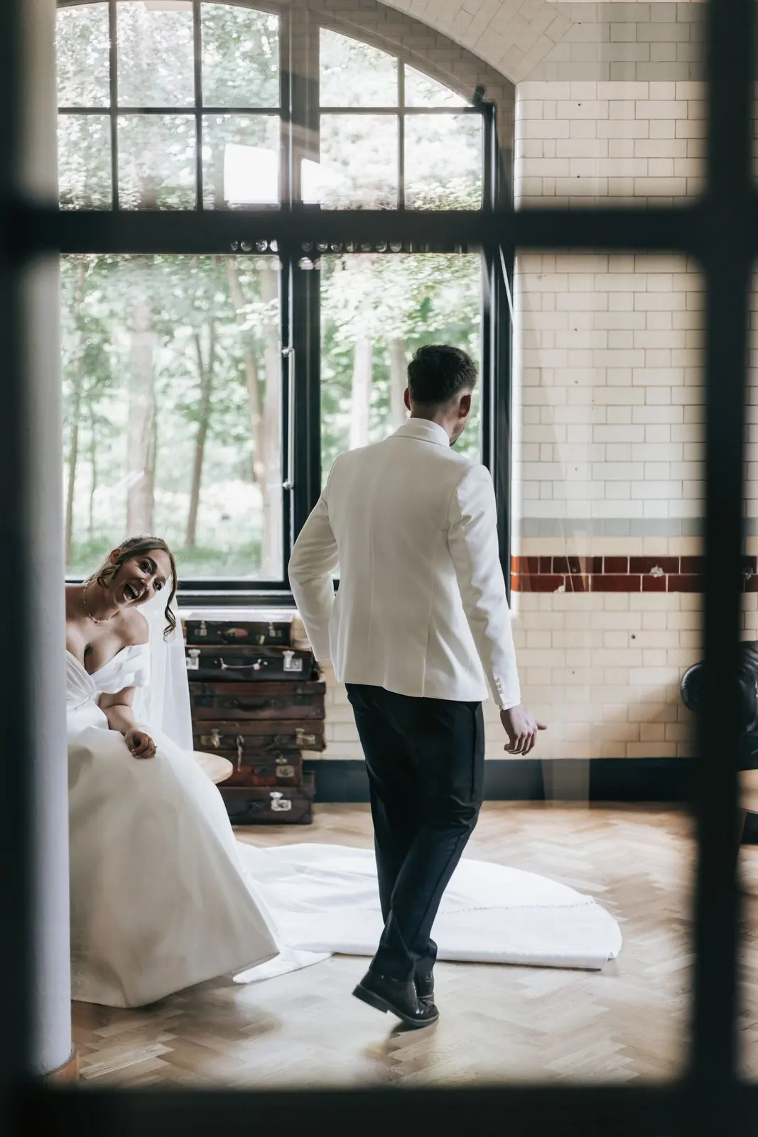Groom seen through a window with the bride's train in the foreground