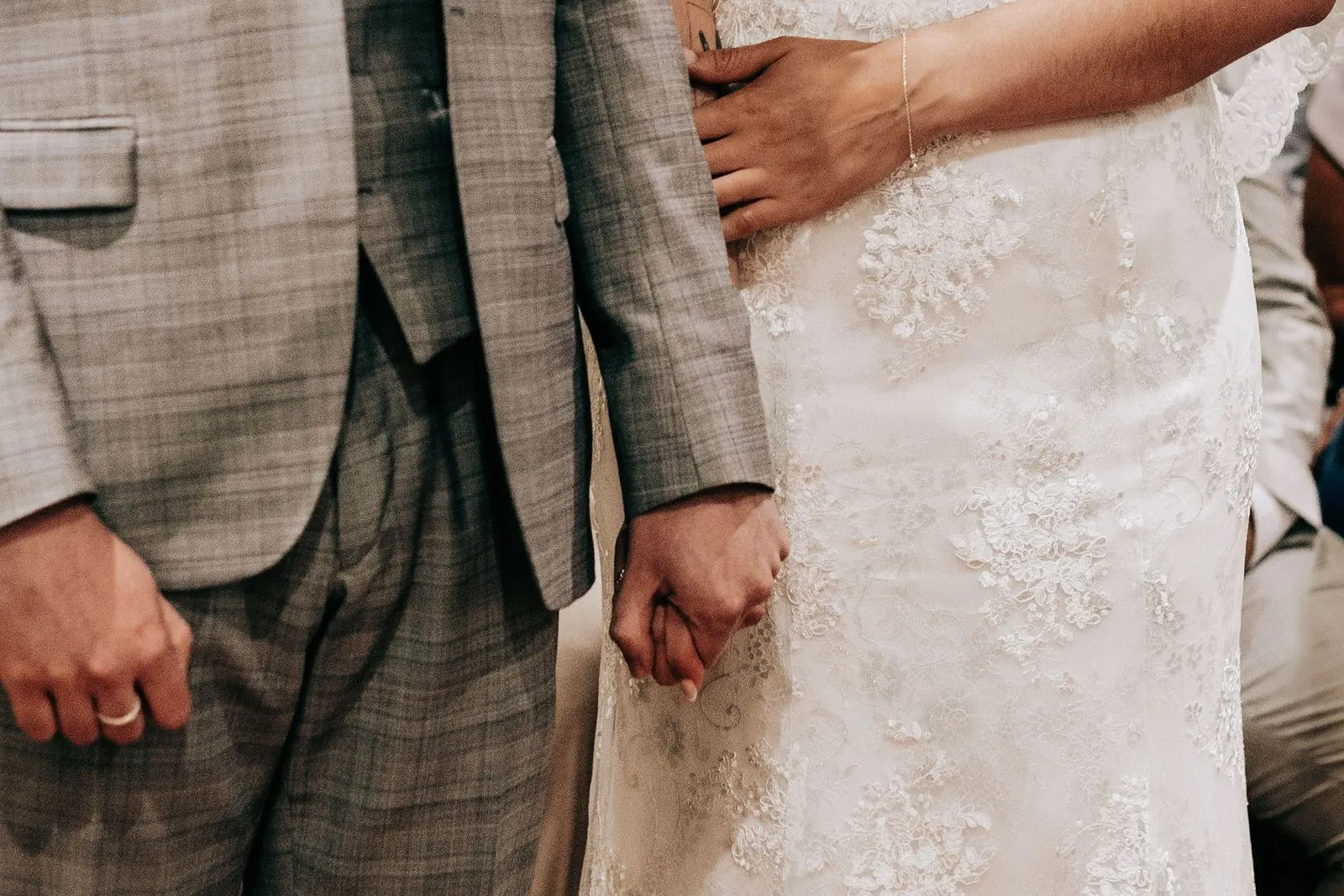 Close detail of the couple's hands and the lace wedding dress