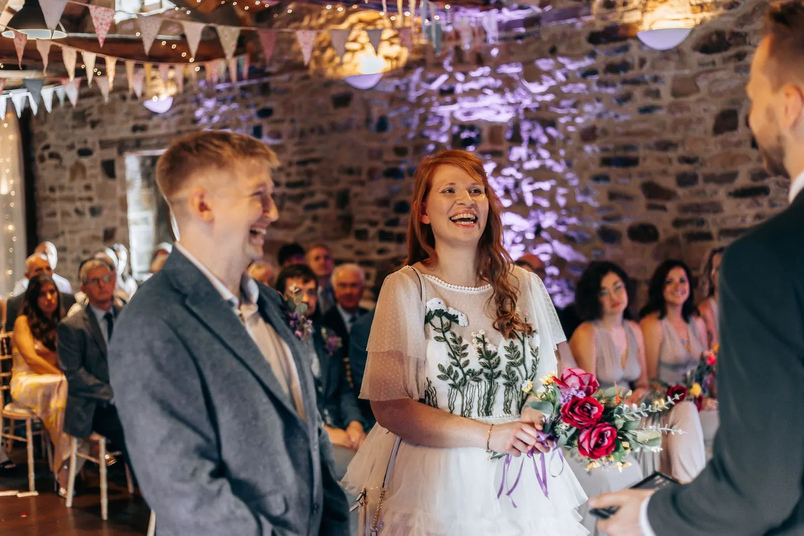 Bride laughing during the ceremony holding a red bouquet