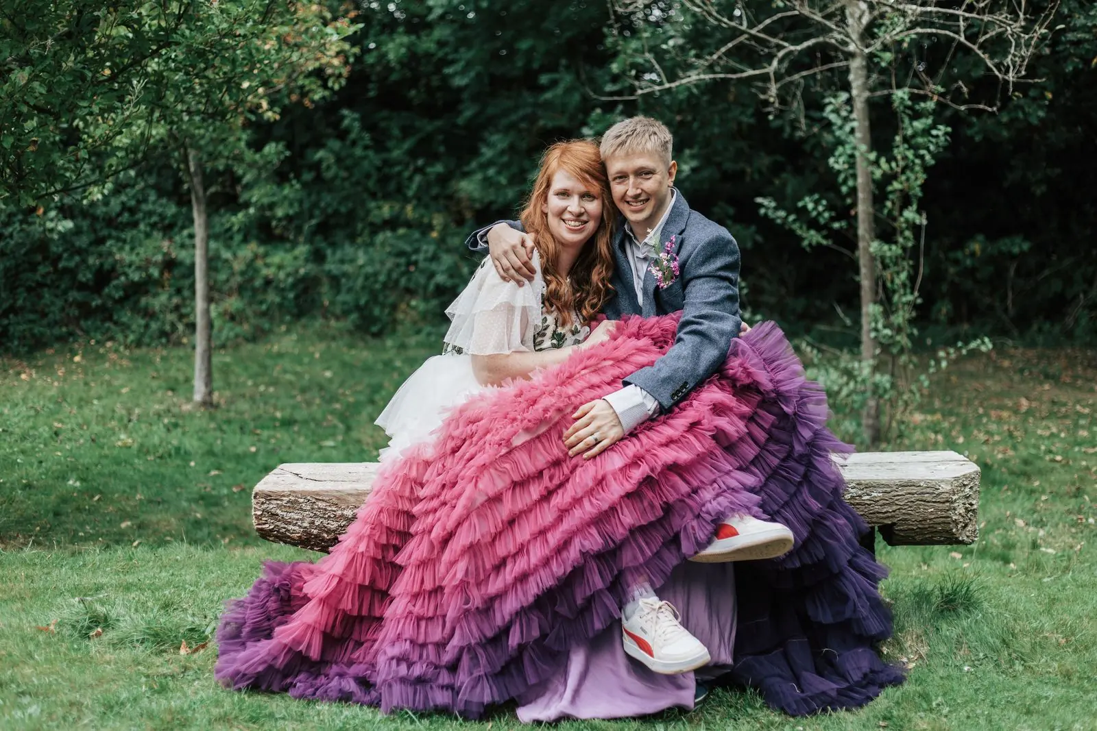 Bride in a pink and purple tulle dress sitting on a bench with her husband