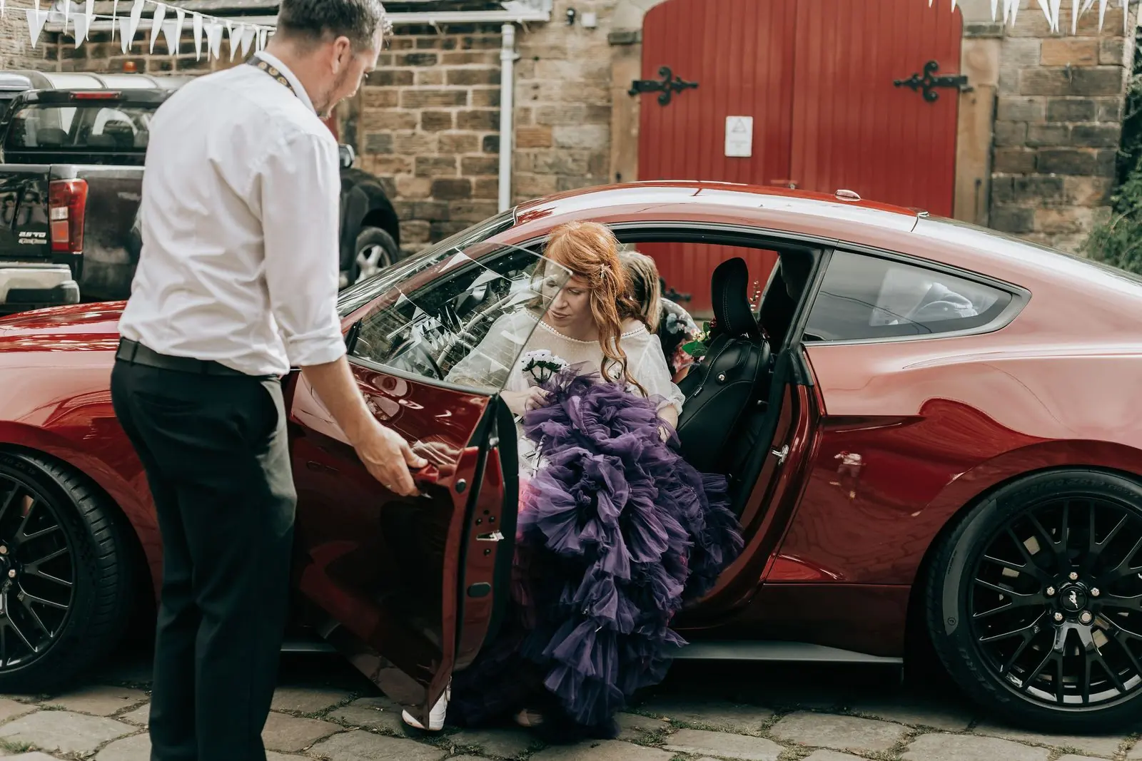 Bride in a purple tulle skirt stepping out of a red car